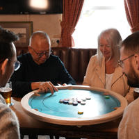 Vier spelers rond het Carrooka Pool 8 Blue draaibord aan een pubtafel, één speler maakt zich klaar voor de stoot