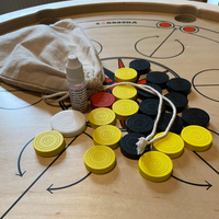 Carrooka Carrom360 fiches in geel, zwart en rood, witte stootsteen, flesje startpoeder en katoenen opbergzakje met trekkoord