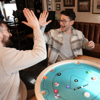 Twee spelers geven elkaar een high five boven het Carrooka Pool 8 Blue draaibord in een pub